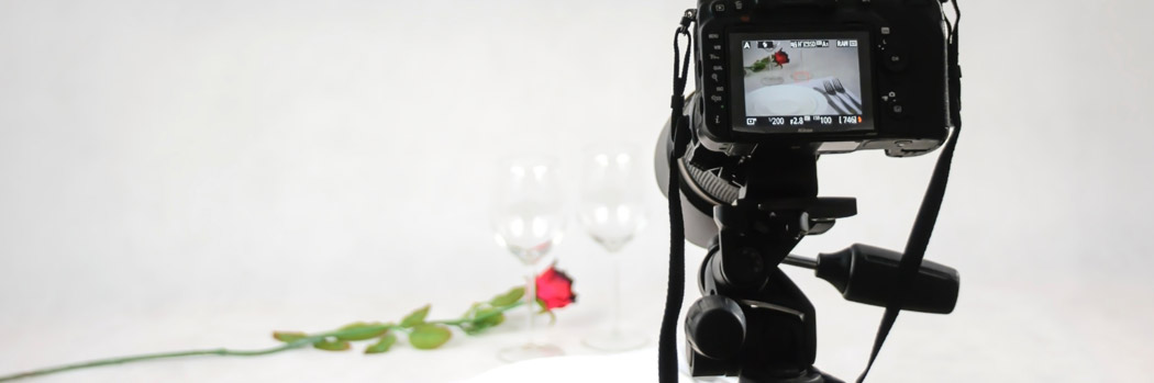 Photography of a camera pointing at a flower and two glasses